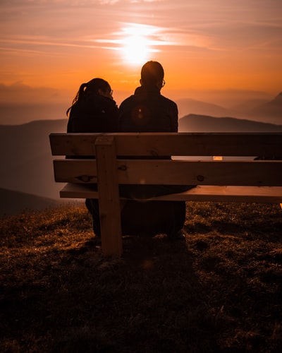 日落时坐在长椅上的两个人的剪影